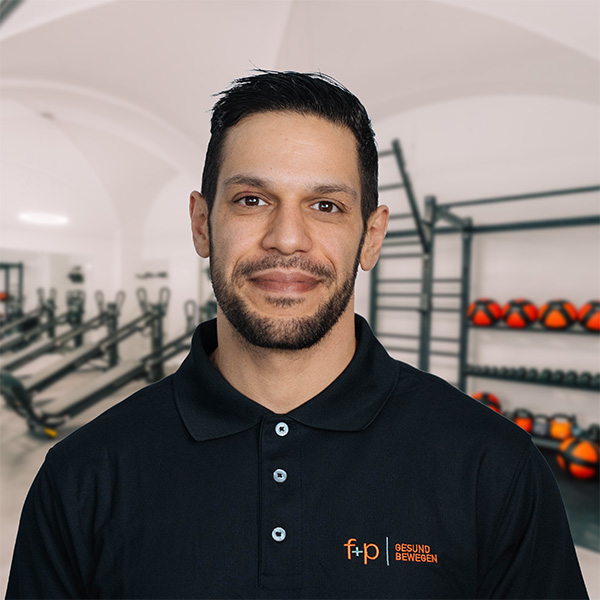ABa Porträt von Amine in einem Fitnessstudio, trägt ein schwarzes Polohemd mit dem f+p Logo, Allgäu-Umgebung ist im Hintergrund sichtbar und Trainingsgeräte prägen das Bild.