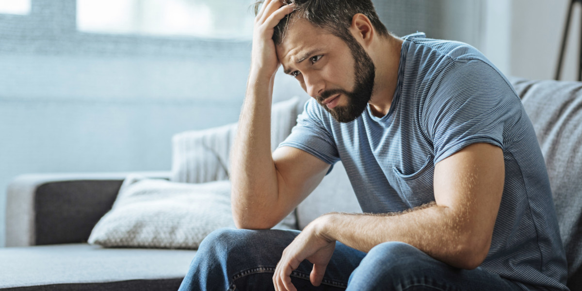 Nachdenklicher Mann mit Hand am Kopf, Stress und Depression auf dem Sofa – psychosomatische Reha ist keine Auszeit, sondern echte Arbeit an sich selbst.