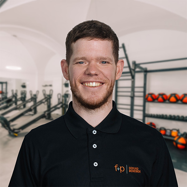 ToFe Tobias in schwarzem Polo vor Trainingsbereich mit Hanteln in der Allgäu-Fitnesspraxis f+p Gesund Bewegen, freundliches Portrait