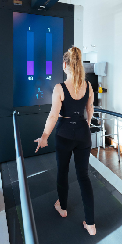 Eine Person läuft auf einer Messplattform, während links und rechts Werte von 48 auf einem blauen Display angezeigt werden.