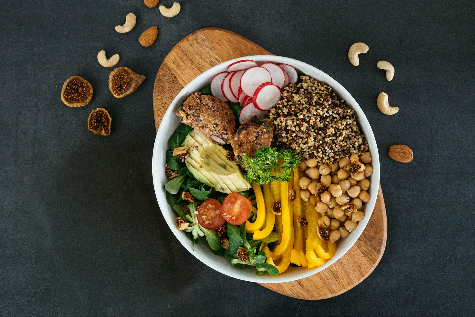 Kochkurse-website2 Bunte Bowl mit Quinoa, Rucola, Paprika, Pilzen, Radieschen und Kräutern auf Holzbrett vor dunklem Hintergrund – gesund kochen.