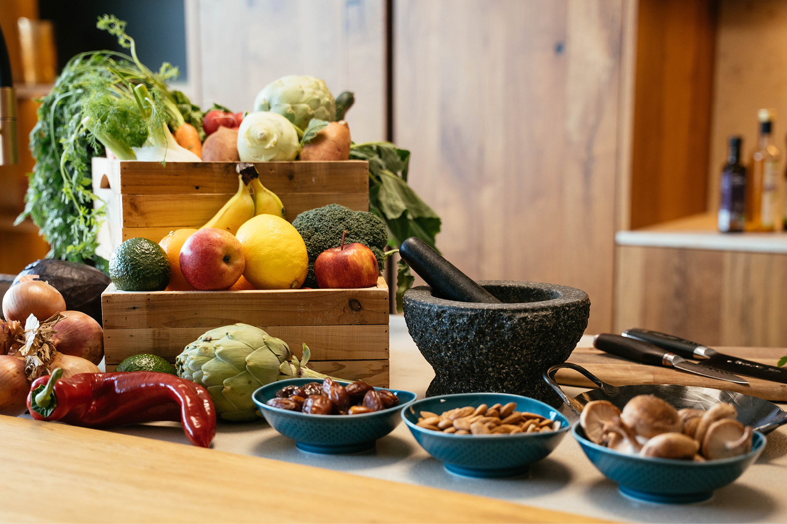 Kochkurse-website4 Frisches Gemüse in einer hölzernen Kiste, daneben Mörser und Schüsseln mit Nüssen – ideal für gesunde Ernährung im Alltag bei Küchen Trunzer.