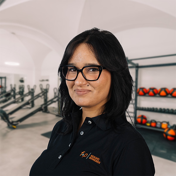 Im Trainingsraum von f+p Gesund Bewegen steht Noura vor Geräten und Medizinbällen mit ruhiger Ausstrahlung, passend zum Bereich Physiotherapie in Kempten.