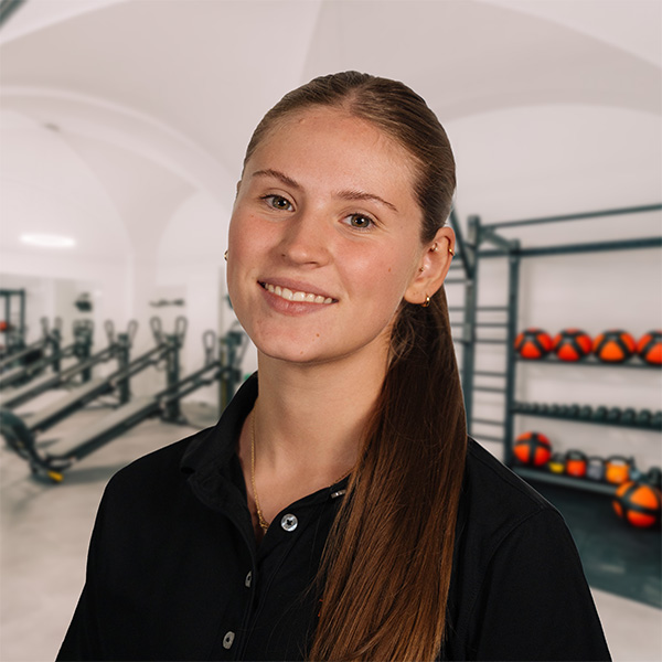 Freundliche Mitarbeiterin Elena mit langen braunen Haaren im schwarzen Poloshirt im Trainingsbereich von f+p Gesund Bewegen