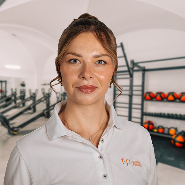 Porträt von Karolina mit braunem Haar und weißem f+p-Poloshirt in einem modernen Fitnessbereich in Kempten