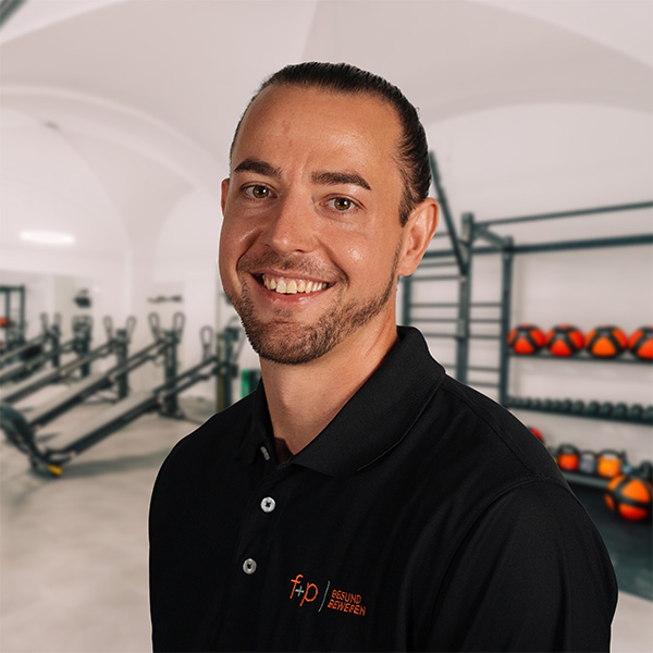 Lächelnder Nino im schwarzen Poloshirt von f+p Gesund Bewegen vor Geräten und Gewichten im Trainingsbereich