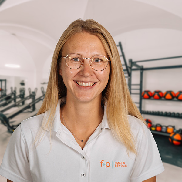 TaDu Freundlich lächelnde Tanja von f+p Gesund Bewegen im weißen Poloshirt vor einem Fitnessbereich in Kempten